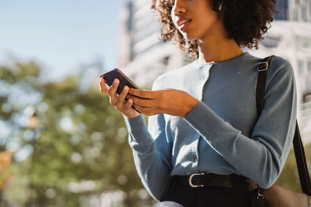 A woman outdoors checking a smartphone in natural daylight.